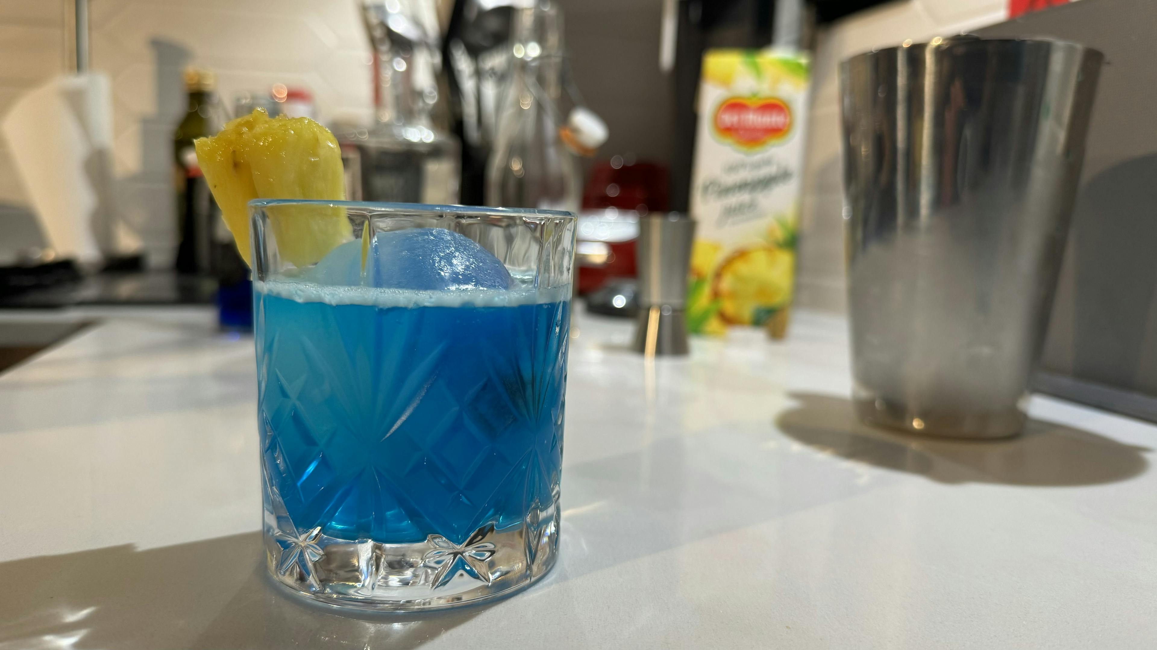 Image of a blue cocktail in a tumblr with a pinapple chunk on its rim
